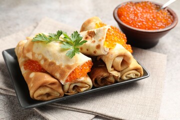 Tasty crepes with red caviar, sour cream and parsley on grey table, closeup