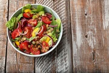 Delicious salad with lentils and vegetables in bowl on wooden table, top view. Space for text
