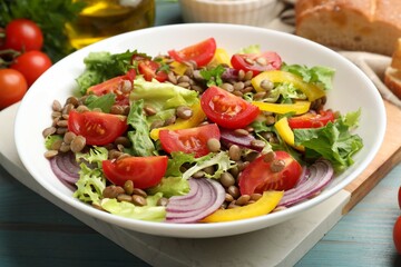 Delicious salad with lentils and vegetables on light blue wooden table, closeup