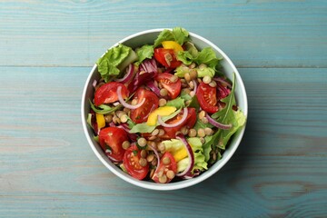 Delicious salad with lentils and vegetables in bowl on light blue wooden table, top view