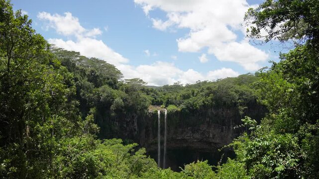 Breathtaking view of a majestic Chamarel waterfall falling into a deep canyon surrounded by dense jungle trees on a bright sunny summer day