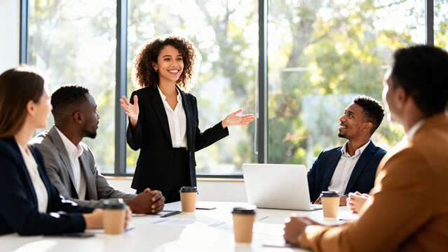 Smiling female leader presenting ideas to a diverse team of colleagues during a collaborative business meeting in a modern office