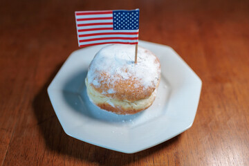 Sweet doughnut topped with powdered sugar and a small American flag on a white plate