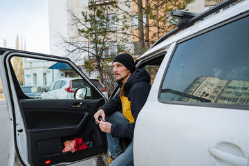 urban man exiting, individual emerges from car onto city sidewalk, man dressed casually with beanie departs vehicle to run brief city errands amid buildings and parked vehicles