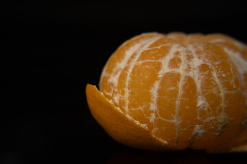 Macro photo of a peeled tangerine on a black background with empty space. Close up citrus texture,...