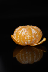 Peeled tangerine on black reflective background, rich in natural vitamin C and antioxidants. Healthy eating and immune support concept with fresh citrus fruit for nutrition, wellness and detox diet.