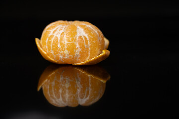 Side view of a peeled tangerine rich in natural vitamin C and antioxidants with reflection on black surface.