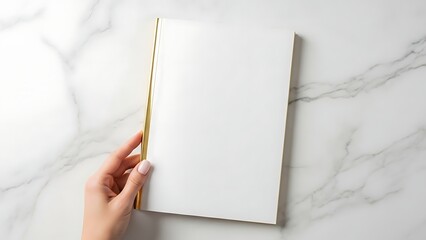Woman's hand holding blank white book on marble background, top view.