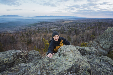 Hiker reaches summit over scenic valley, Accomplishing outdoor adventure along jagged mountain path, Fulfillment felt by daring ascent over dramatic rocky terrain into lush green wilderness