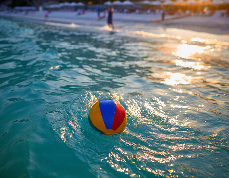 A vibrant beach ball floats in turquoise ocean water, bathed in golden sunlight. Evokes carefree summer days, vacations, and the joy of seaside recreation.