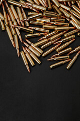 A scattering of shiny brass rifle cartridges with copper-tipped bullets on a black back