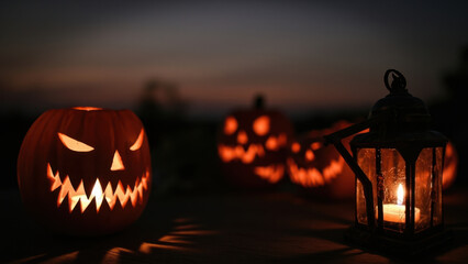 Spooky Halloween pumpkins with carved faces and a glowing candle lantern at dusk