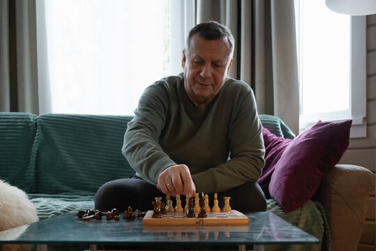 Focused senior man sitting at home playing chess, enjoying a calm indoor activity and thoughtful leisure time. Home Leisure Activities - Powered by Adobe