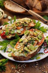 Broad bean spread sandwiches with and grilled goat cheese sprinkled with roasted sunflower seeds and fresh mint on a ceramic plate, close-up 