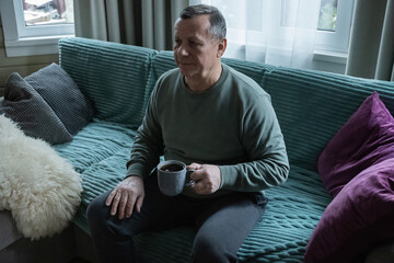 Relaxing senior caucasian man sitting on sofa with coffee drink, enjoying calm moment indoors in cozy home setting. Home Leisure Activities