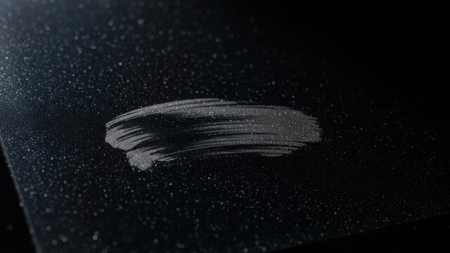 Graphite powder creates sleek smudge on black surface, capturing minimalist aesthetic. Smudge highlights texture and subtle sheen of powder in dim light.