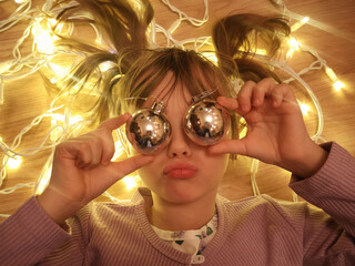 A funny portrait of a girl with Christmas tree decorations against the backdrop of a Christmas tree garland.