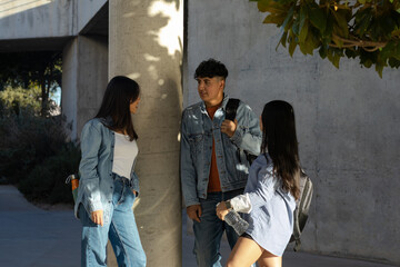 Three diverse young adult students, carrying backpacks, engaging in a casual conversation and...