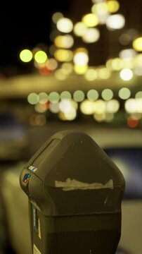 Streetlights illuminate a quiet city road, creating a dreamy atmosphere at night. A parking meter stands in focus, while blurred vehicles and lights enhance the tranquil vibe of the scene.