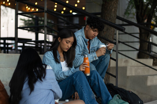 Young adult friends sitting on urban stairs, sharing a casual social gathering, connecting and relaxing in a relaxed outdoor environment - Powered by Adobe