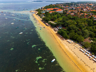 Aerial drone view of the tropical coastline of Sanur in Bali with boats and resorts