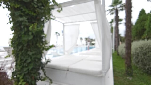 The hazy background showcases opulent poolside cabanas, adorned with billowing white curtains swaying in the warm summer air. A peaceful setting at a tropical retreat