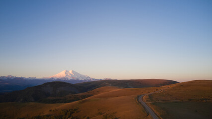 Autumn mountain landscape. A winding road across a mountain plateau with a snow-capped volcano in the distance. Drone footage.