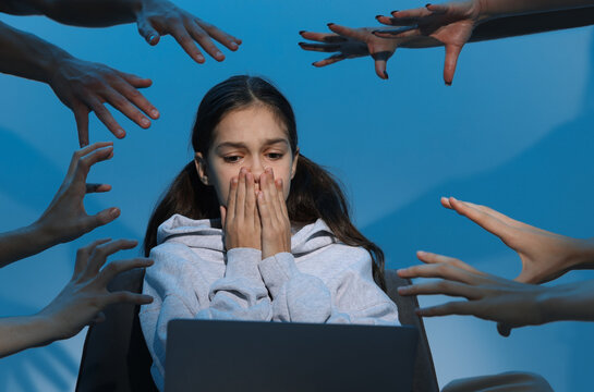 Cyber danger. Frightened girl using laptop while hands reaching towards her on blue background