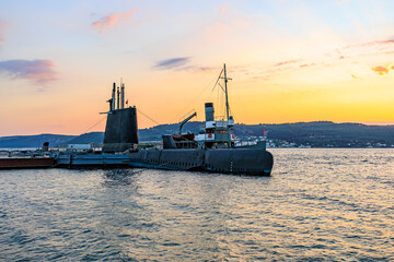 Fototapeta premium Historic military submarine and naval ship at sunset in tranquil harbor