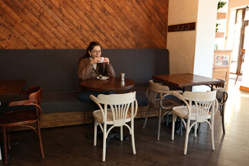 Young woman in glasses drinking tea at a table in a cafe