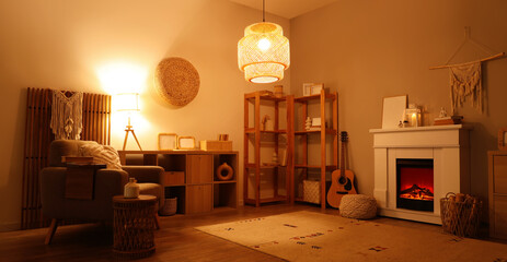 Fototapeta premium Interior of living room with fireplace, armchair and glowing lamps in evening