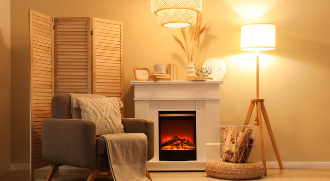 Interior of cozy living room with fireplace, armchair and glowing lamps