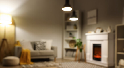 Fototapeta premium Blurred view of living room with fireplace, sofa and glowing lamps in evening