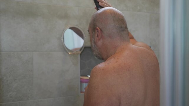older man shaving his head with an electric razor in the shower