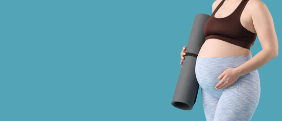 Sporty young pregnant woman with yoga mat on blue background, closeup