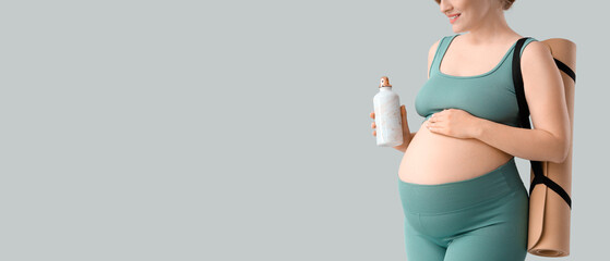 Sporty young pregnant woman with yoga mat and sports bottle on grey background