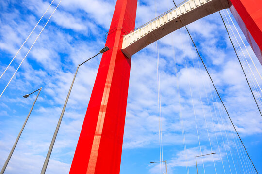 Red suspension bridge against blue sky and clouds with streetlights