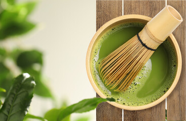 Naklejka premium Matcha tea and whisk in cup on wooden table against green leaves