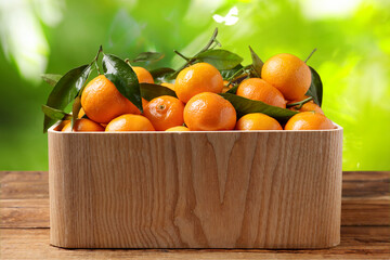 Fresh juicy tangerines in crate on wooden table against blurred green background