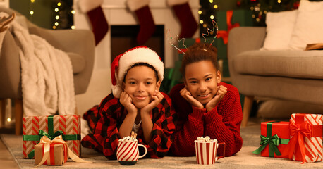 Happy African-American children with cocoa and presents lying at home on Christmas eve