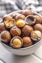 Tasty macadamia nuts in bowl on white table.