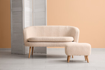 Cozy white sofa with ottoman and folding screen near beige wall