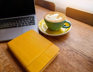 a bright yellow notebook and matching coffee cup with latte art sit on a laptop and wooden table creating a vibrant workspace scene