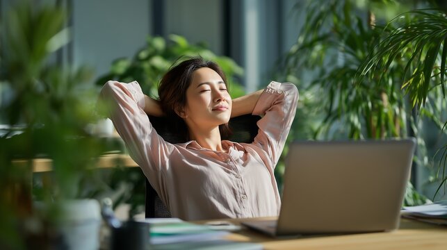 Relaxed businesswoman taking break at modern office desk with laptop and plants