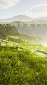 Morning light spills over the rolling hills of a vast green valley, illuminating the textures of grass and rock.