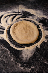 Freshly Shaped Pizza Dough Ready for Tomato Sauce on a Floured Kitchen Counter.