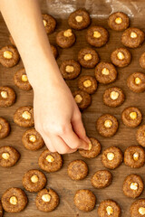 Top view of a child's arm reaching to place a hazelnut on a raw cookie. Christmas baking preparation