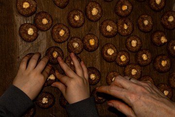 Top view of woman and child hands decorating hazelnut cookies on a tray. Family baking tradition and teaching moments