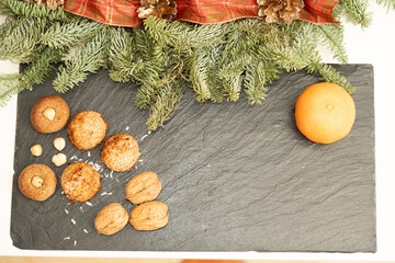 Festive flat lay with coconut macaroons, nuts, mandarin and fir branches on a black slate board with copy space