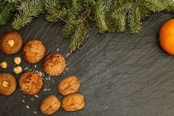 Top down view of homemade coconut macaroons and hazelnut cookies arranged on a dark slate plate with walnuts and pine branches framing the scene